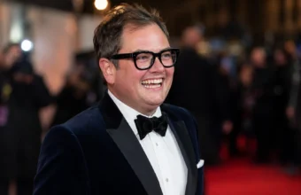 Alan Carr smiling in a formal tuxedo at a red-carpet event for an article about his 2026 net worth.