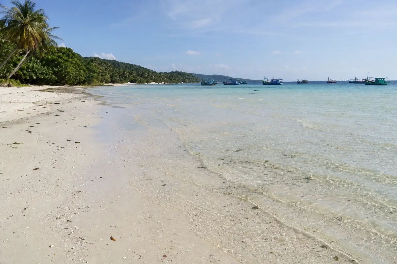 Bai Sao Beach in Phu Quoc with white sand, clear turquoise water, palm trees, and fishing boats offshore