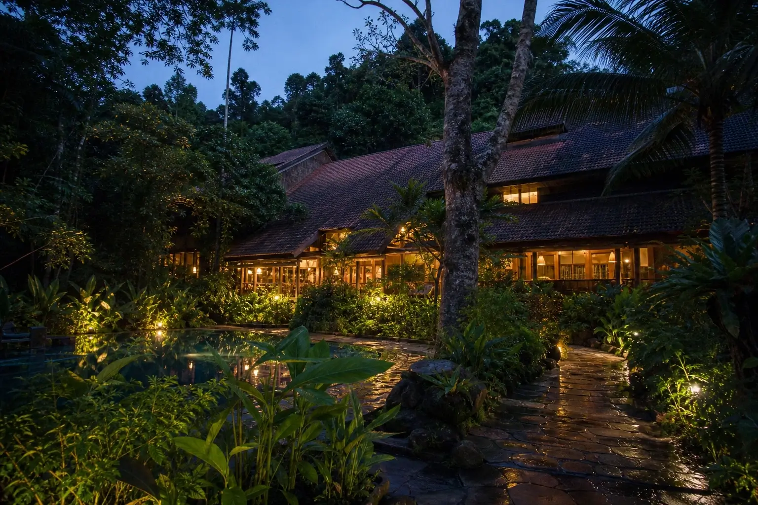 Cat Tien Jungle Lodge at dusk surrounded by rainforest with warm lights, pool, and stone walkway in Vietnam