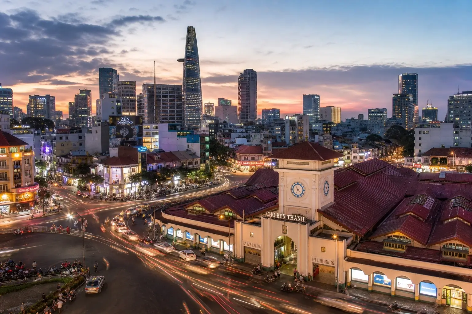 Ben Thanh Market and Ho Chi Minh City skyline at dusk with evening traffic light trails.