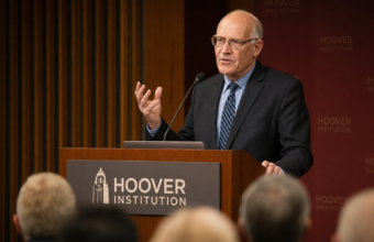 Speaker at a Hoover Institution-style podium during a public forum, used to illustrate Howard Lorber net worth estimates.