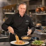 Italian chef in a black chef jacket cooking pasta in a professional restaurant kitchen