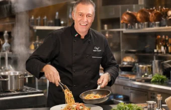 Italian chef in a black chef jacket cooking pasta in a professional restaurant kitchen