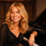 Karen McCollum seated beside a grand piano in a formal black outfit.