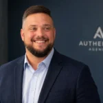 Mike Nellis professional headshot in navy blazer with Authentic Agency background