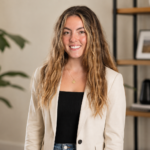 Woman in a cream blazer smiling in a modern office setting for a Mila Volovich creator profile.