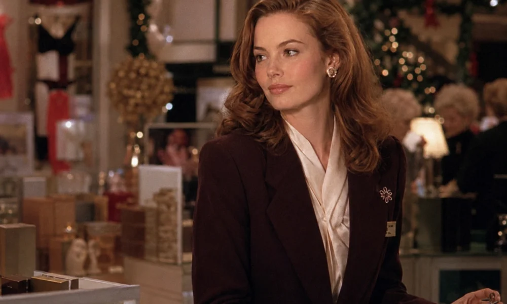 Elegant auburn-haired saleswoman in a burgundy blazer at a festive 1980s department-store counter.