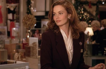 Elegant auburn-haired saleswoman in a burgundy blazer at a festive 1980s department-store counter.
