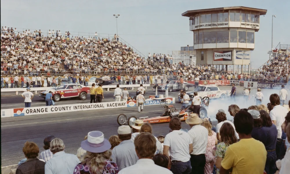 1970s drag racing event at Orange County International Raceway with packed crowds, vintage drag cars, and race-day smoke.