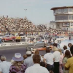 1970s drag racing event at Orange County International Raceway with packed crowds, vintage drag cars, and race-day smoke.