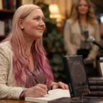 What Rebecca Yarros Is Actually Worth And the Numbers That Explain It Rebecca Yarros signing books at a literary event with stacked novels and a microphone.