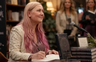 Rebecca Yarros signing books at a literary event with stacked novels and a microphone.