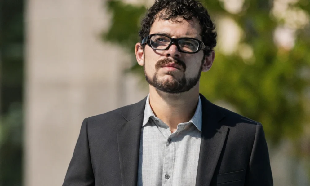 Rodrigo Blankenship wearing glasses and a dark suit outdoors.