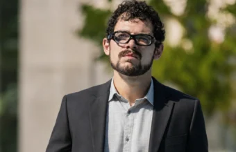 Rodrigo Blankenship wearing glasses and a dark suit outdoors.
