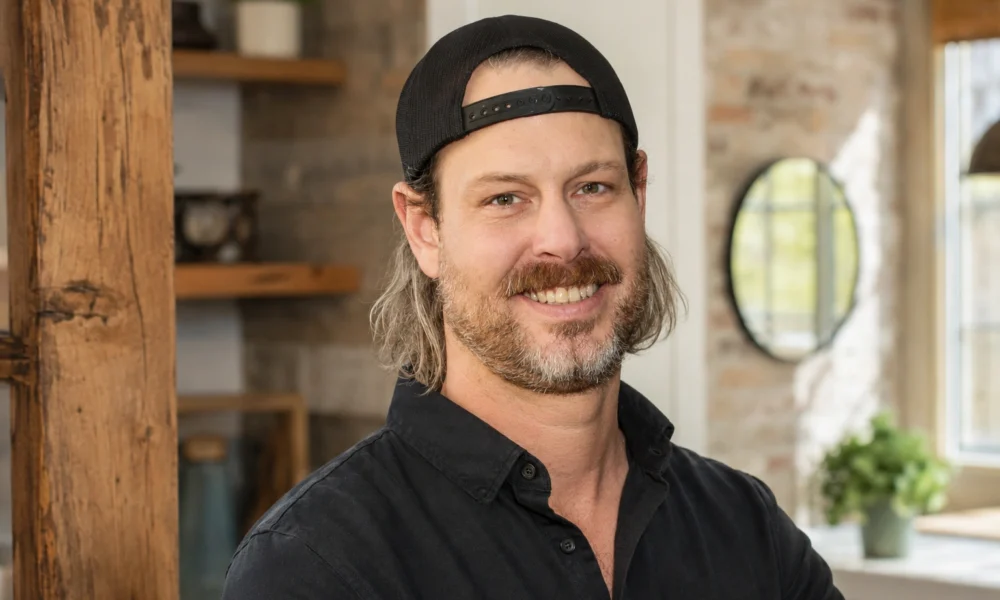 Steve Ford smiling in a black shirt and backward cap inside a renovated home interior.