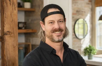 Steve Ford smiling in a black shirt and backward cap inside a renovated home interior.