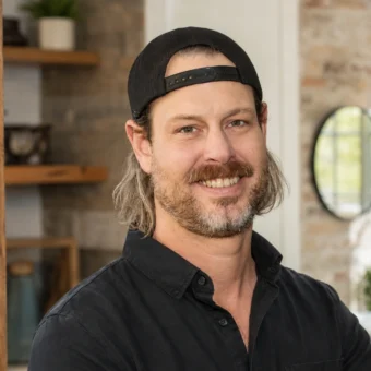 Steve Ford smiling in a black shirt and backward cap inside a renovated home interior.