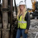 Vanessa Lucido wearing a hard hat and safety vest beside drilling equipment at a construction site