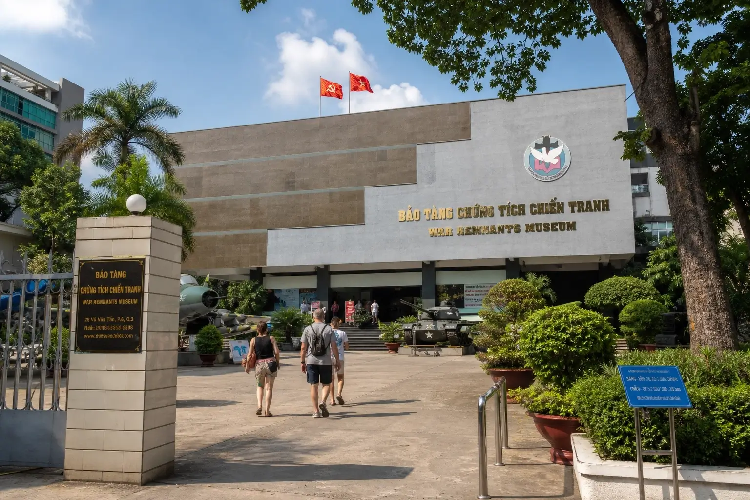 War Remnants Museum exterior in Ho Chi Minh City, Vietnam with entrance sign, visitors, trees, and military displays.