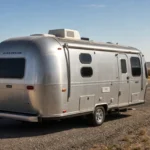 Silver Airstream Bambi travel trailer parked beside a desert highway under a clear blue sky.