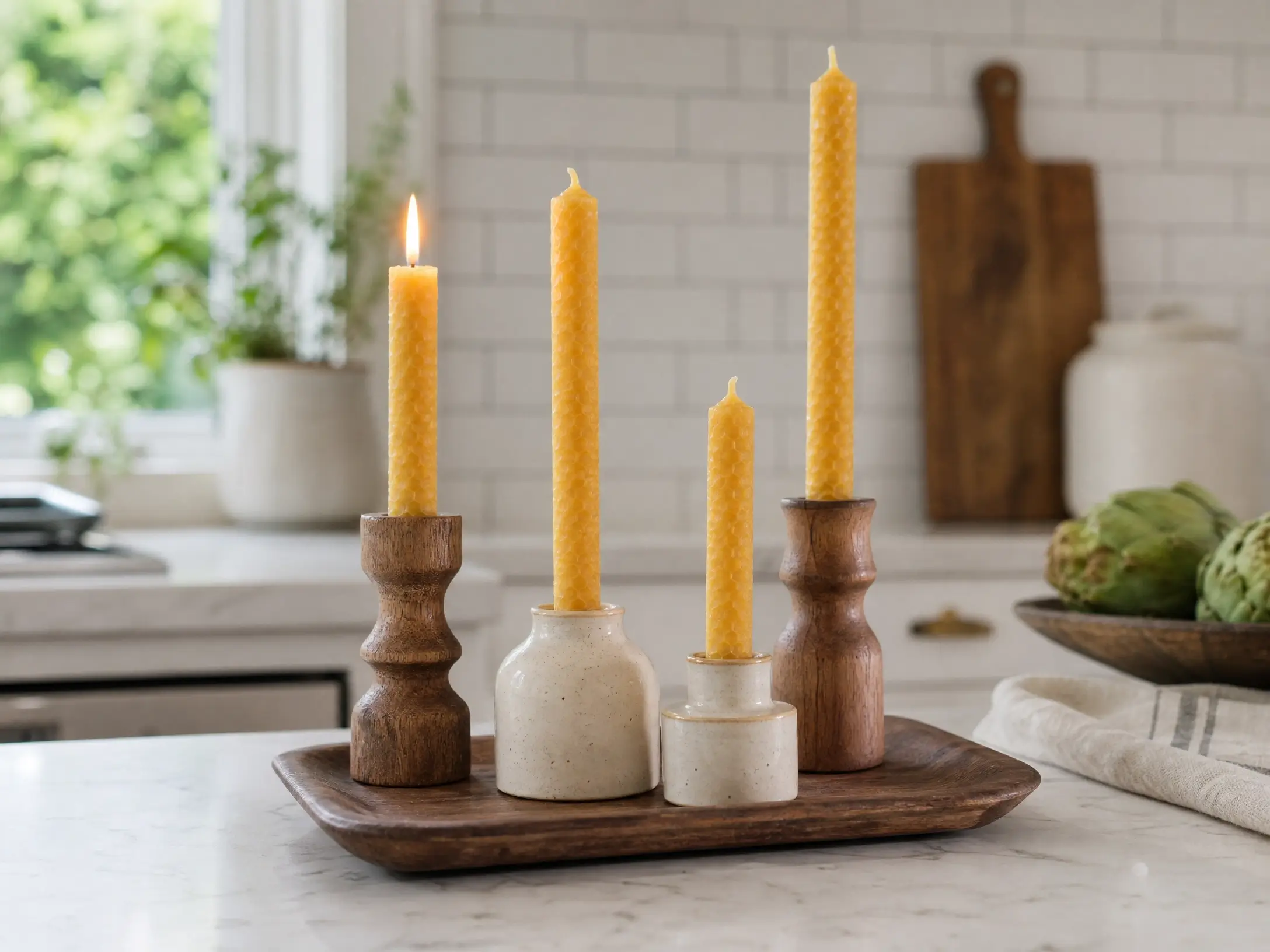 Beeswax taper candle vignette in wood and ceramic holders on a cozy kitchen counter.