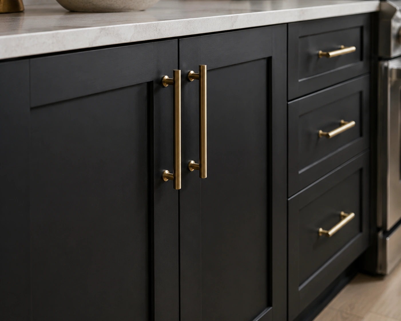 Brushed brass handles on matte black shaker cabinet fronts with a light stone countertop