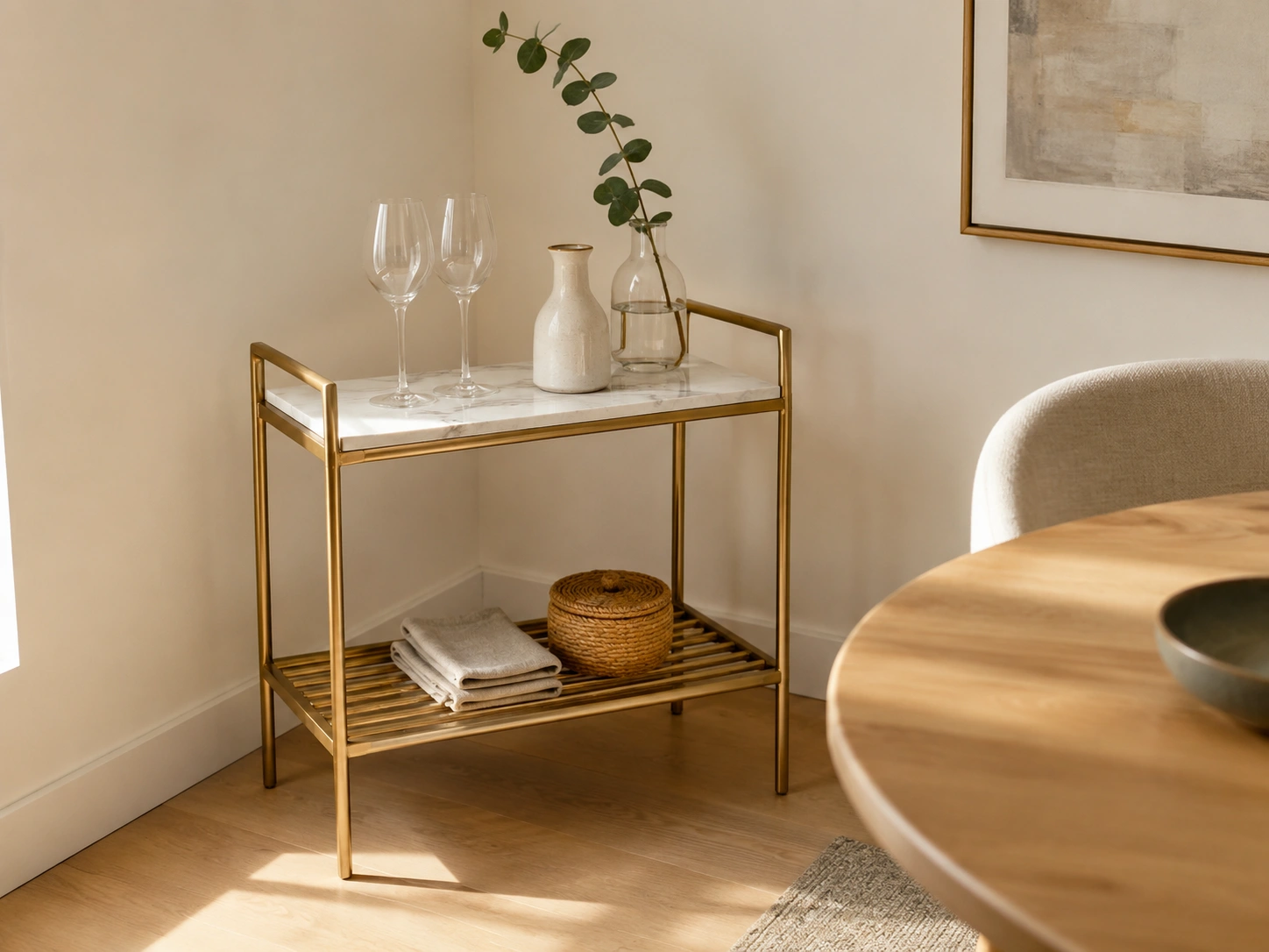 Brushed gold two-tier bar cart with marble top styled in a warm small dining room corner.