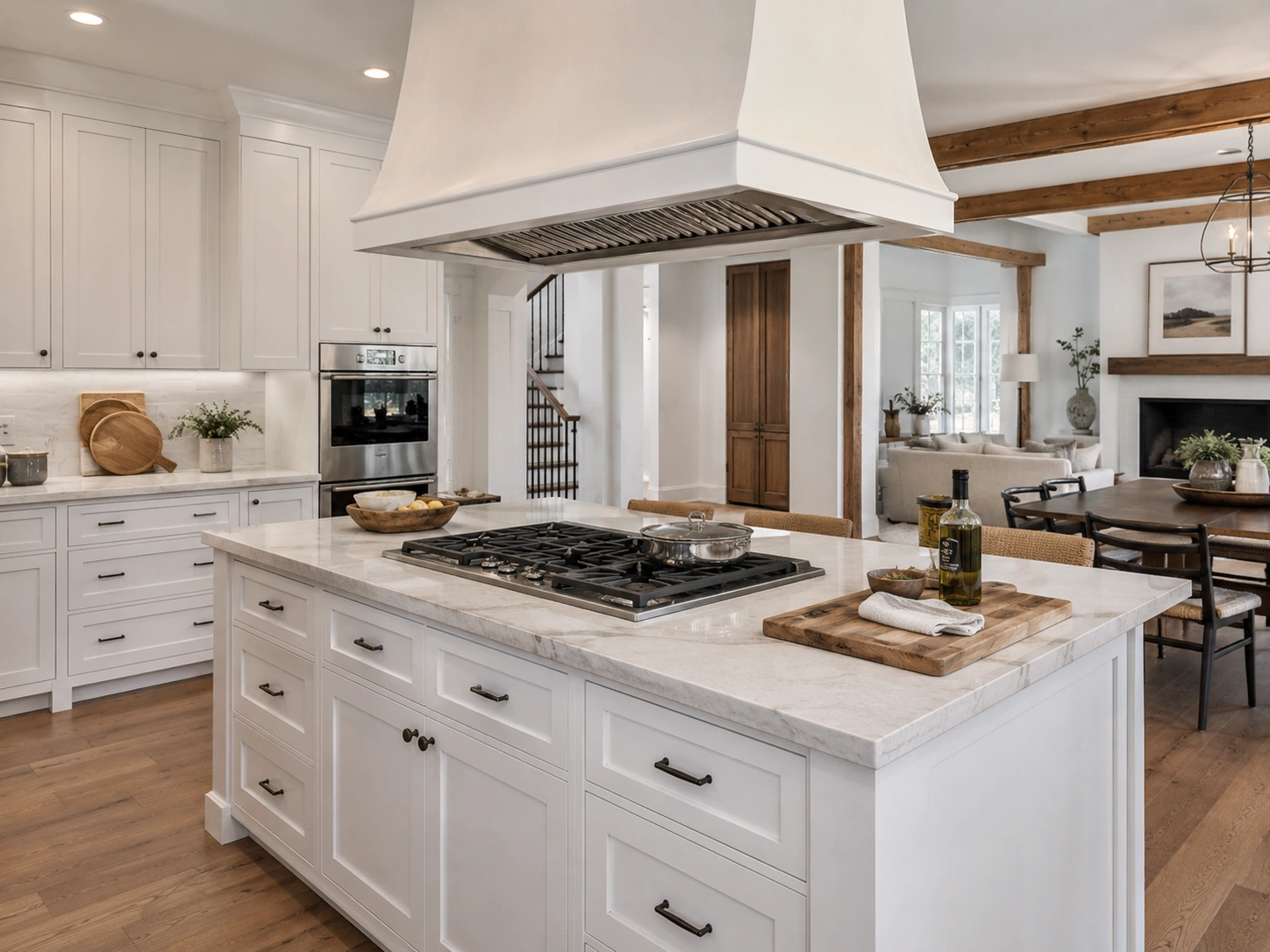 White kitchen island with built-in gas cooktop and large overhead statement hood.