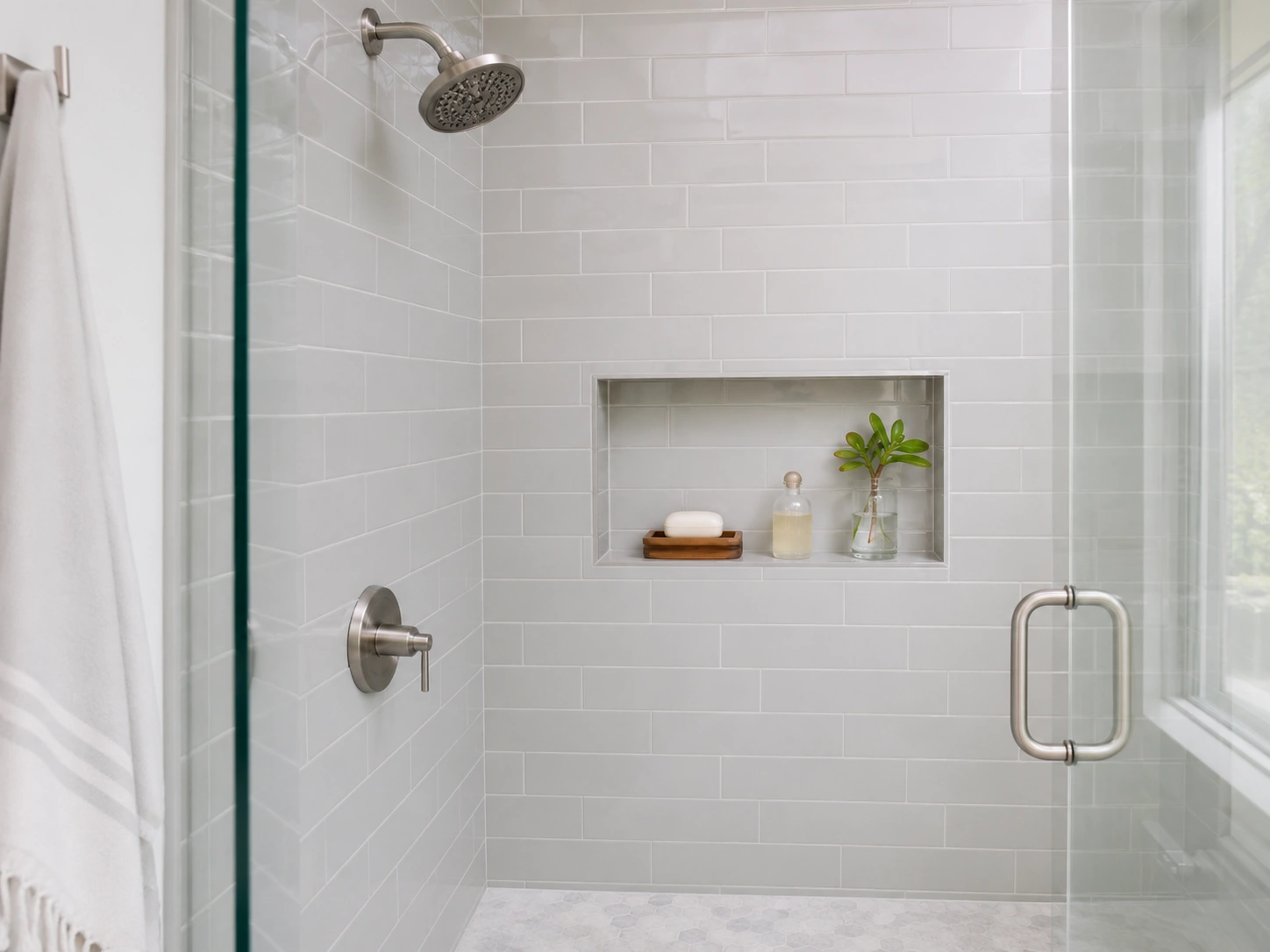Built-in shower niche shelf with soap, bottle, and small plant in a white subway tile bathroom shower.