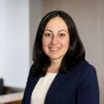 Cheryl Irwin professional portrait in navy blazer in a modern office setting.