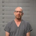 Mugshot of Erik Neel standing in front of a police height scale showing measurements from 3'0" to 6'0".