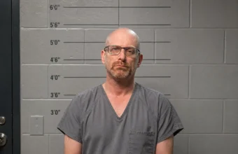 Mugshot of Erik Neel standing in front of a police height scale showing measurements from 3'0" to 6'0".