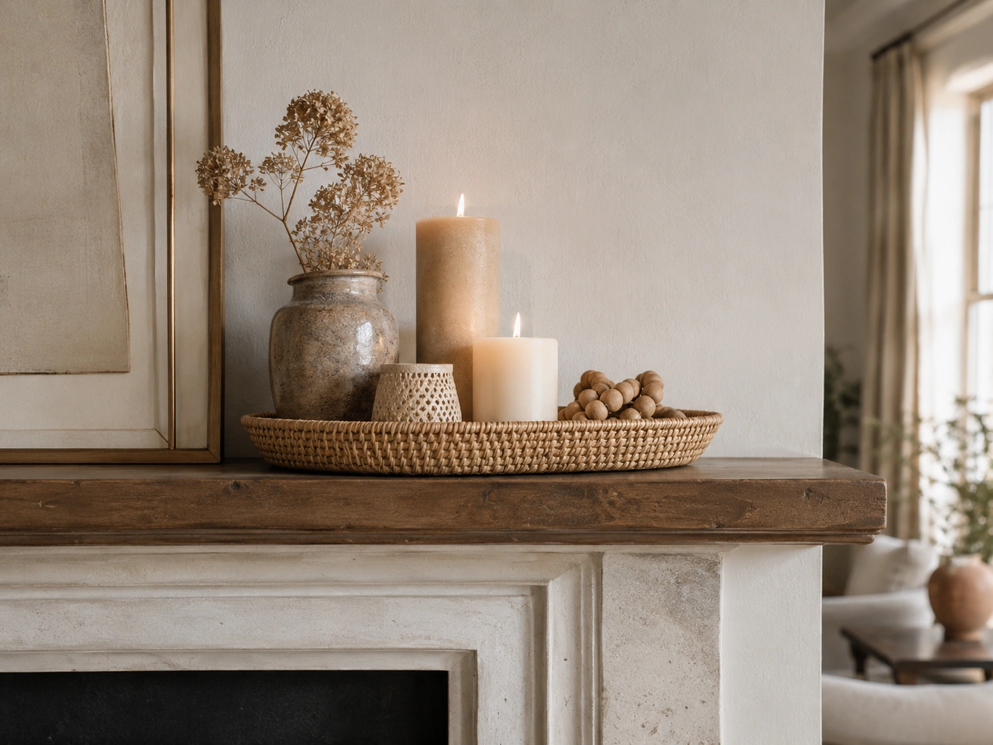 Flat woven tray with candles, ceramic vase, dried flowers, and beads on a rustic fireplace mantel