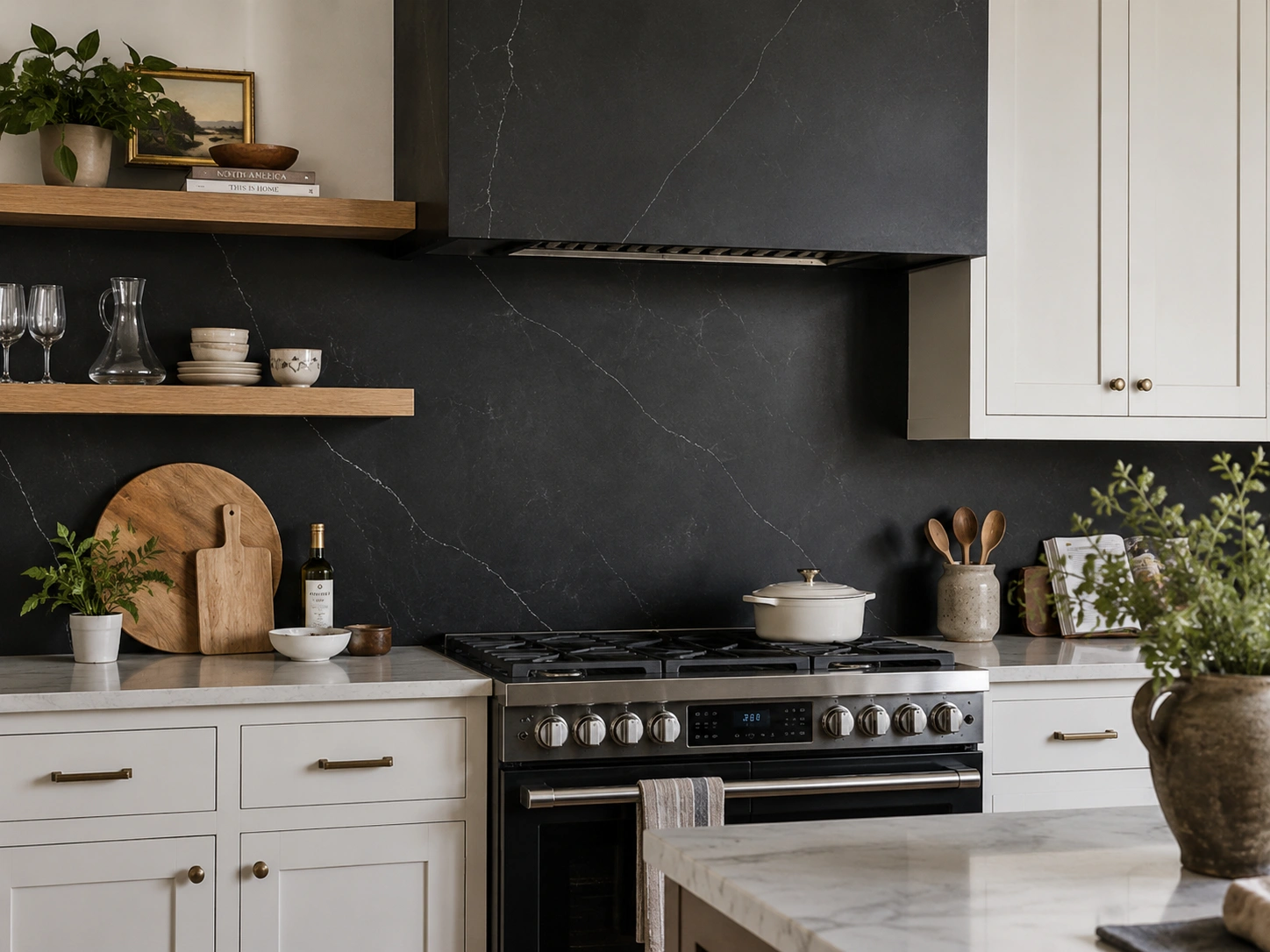 Honed black marble range wall with white cabinets, oak shelves, brass hardware, and a marble kitchen island.