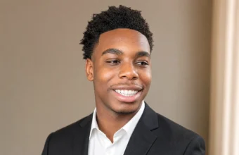 Isaiah Dickerson smiling in a black suit and white shirt against a neutral indoor background.