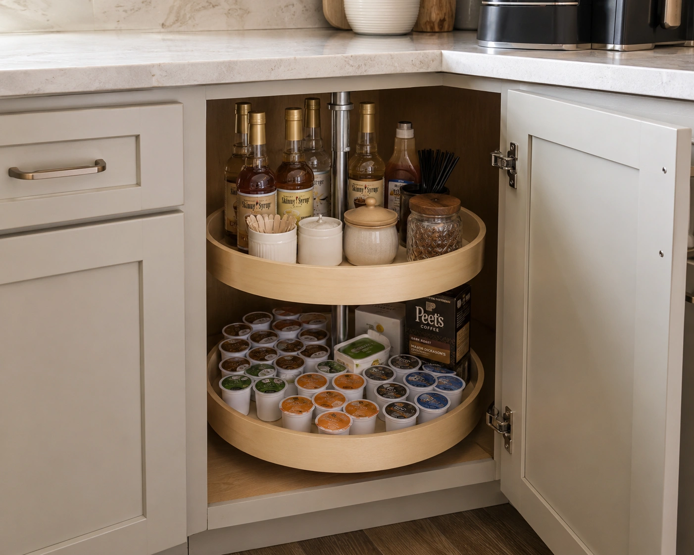 Lazy Susan coffee pod carousel inside a corner kitchen cabinet with syrups and supplies.
