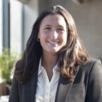 Macy Piersiak smiling in a black blazer and white shirt in a bright office setting.