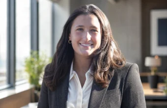 Macy Piersiak smiling in a black blazer and white shirt in a bright office setting.