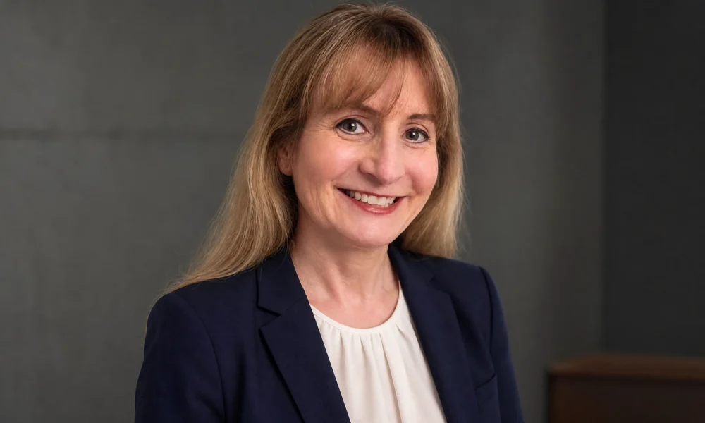 Margot Cleveland smiling in a navy blazer against a gray studio background