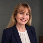 Margot Cleveland smiling in a navy blazer against a gray studio background