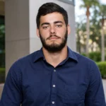 Mark Piccirillo in Tampa outdoor portrait wearing a navy shirt near palm trees and a modern building.