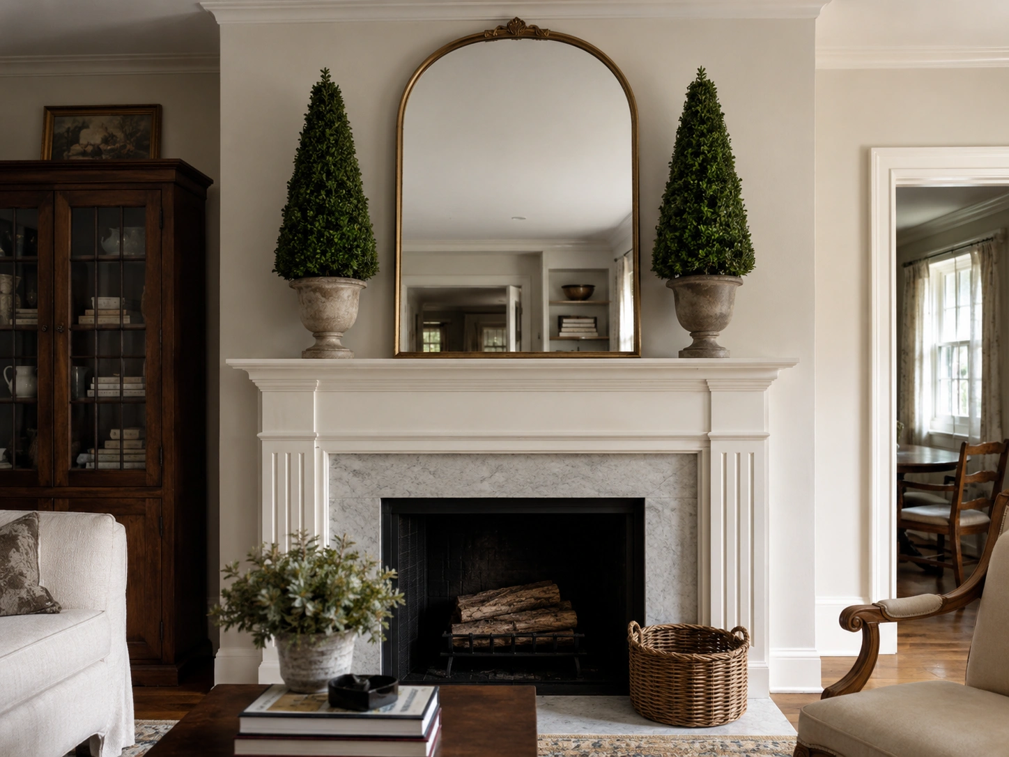 Traditional mantel with matching potted topiaries, gallery wall art, black fireplace, and rustic wood beam.