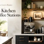 Modern kitchen coffee station with espresso machine, open wood shelves, mugs, plants, and soft natural light.