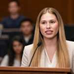 Olivia Krolczyk speaking into a microphone during a formal campus event with audience members in the background