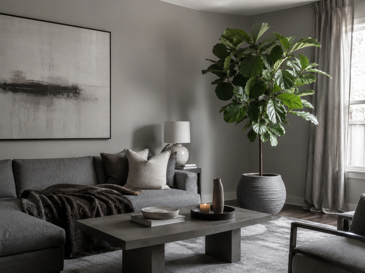 Oversized statement plant beside a grey sofa in an all-grey living room with soft curtains.