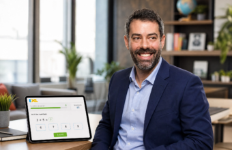 Paul Mishkin seated in an office beside a tablet showing an IXL math question