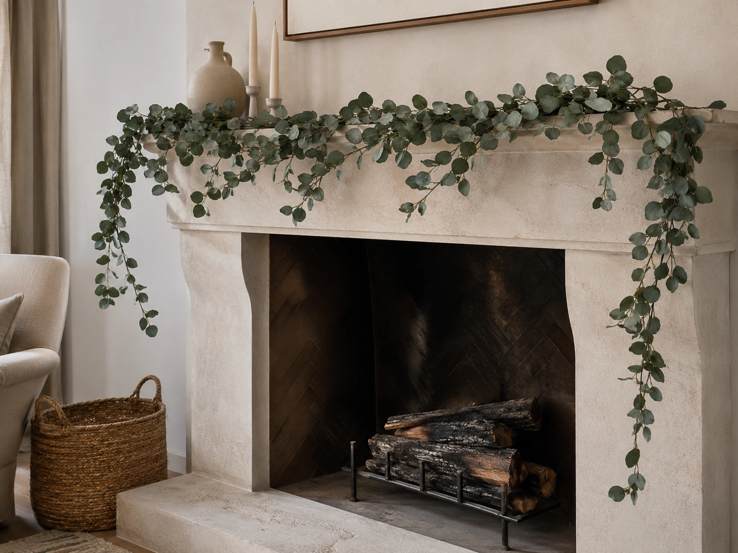 Preserved eucalyptus garland draped along a neutral stone fireplace mantel with candles and ceramic vase.