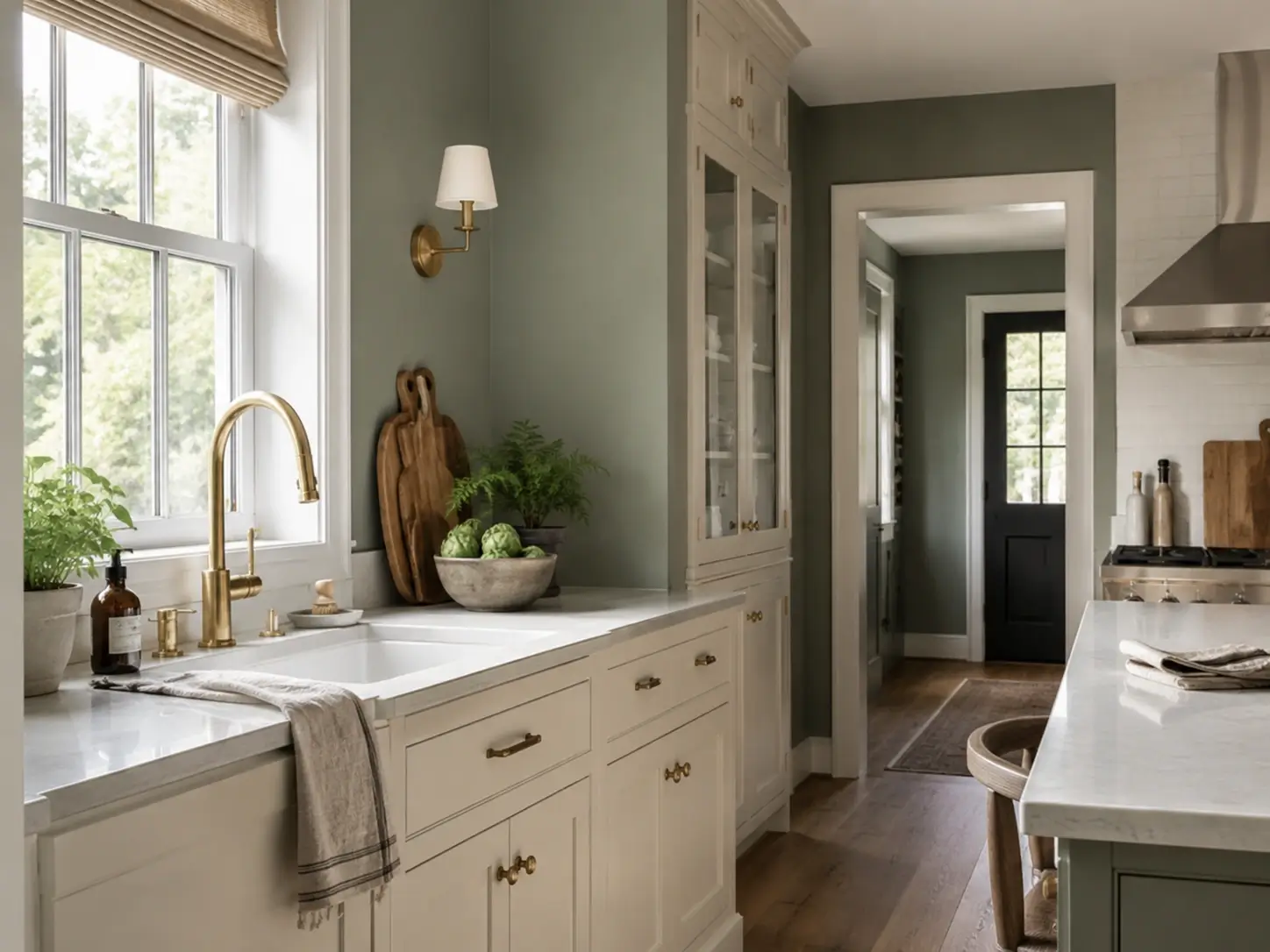 Sage green kitchen with cream cabinets, unlacquered brass hardware, brass faucet, marble counters and warm wood floors