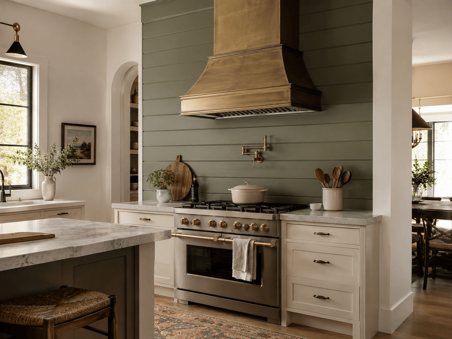 Sage green shiplap range wall with brass hood, cream cabinets, marble counters, and built-in stove