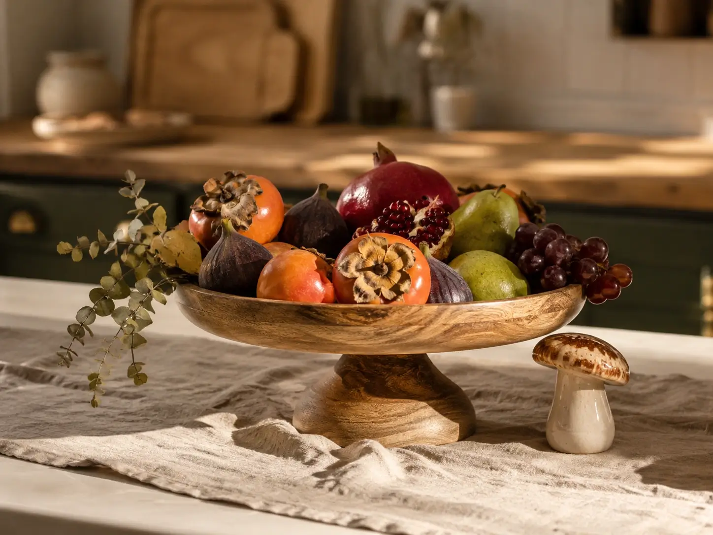 Wooden fruit bowl styled like a still life with figs, pomegranate, pears, grapes and persimmons on a kitchen counter.